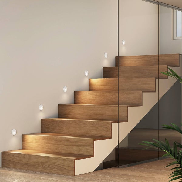 Moderne Holztreppe mit runden LED-Einbauleuchten zur Stufenbeleuchtung an der Wand, Glasgeländer und helles Design.