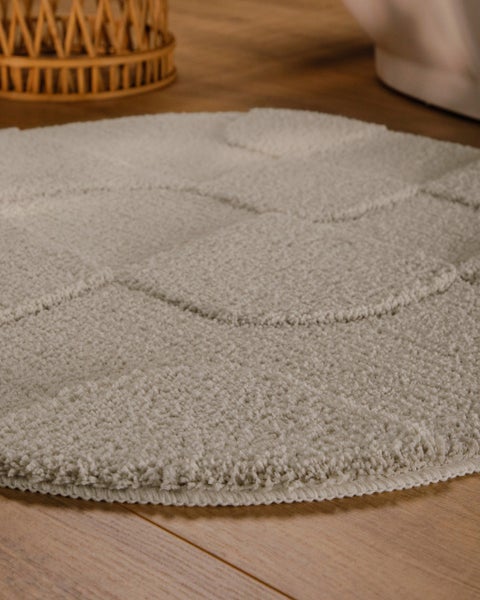 Runder beiger Badteppich mit Hoch-Tief-Struktur und kreisförmigem Muster auf Holzboden.