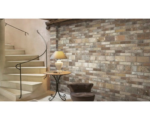 Wand mit Riemchen in Ziegeloptik neben einer Treppe mit schmiedeeisernem Geländer, Beistelltisch mit Lampe und einem Sessel im Innenraum.