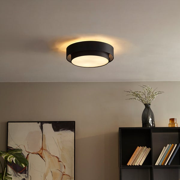 Moderne runde Deckenleuchte mit schwarzem Metallrahmen und weißem Diffusor in einem Wohnzimmer.