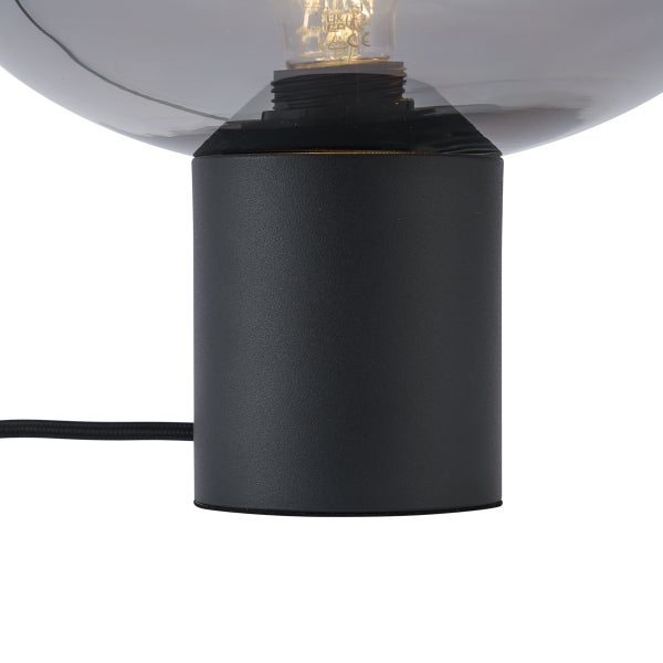 Nahaufnahme eines schwarzen zylindrischen Tischlampensockels mit rauchfarbenem Glasschirm und Leuchtmittel.