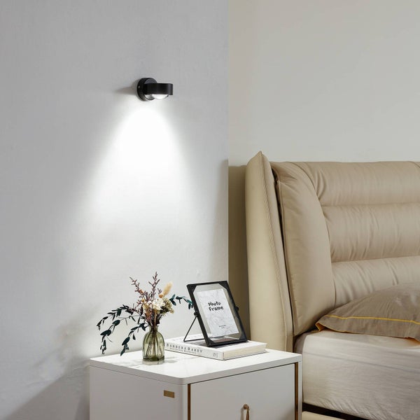 Schlafzimmer Szene mit einer schwarzen Wandleuchte, einem Nachttisch, einer Blumenvase und einem Bilderrahmen.