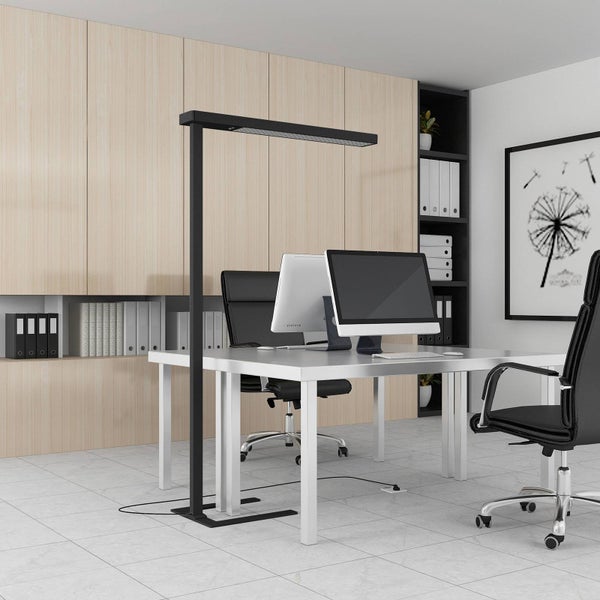 Moderne LED-Stehleuchte an einem hellen Büroarbeitsplatz mit Schreibtisch, Monitoren und Bürostuhl vor einer organisierten Holzschrankwand.