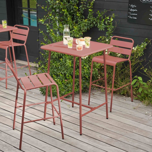 Modernes Gartenmöbel-Set bestehend aus einem quadratischen Stehtisch und Barstühlen aus Metall in Rostrot auf einer Holzterrasse.
