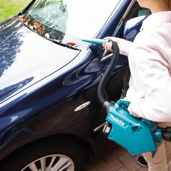 Eine Person reinigt ein Auto mit einem Akku-Staubsauger der Marke Makita.