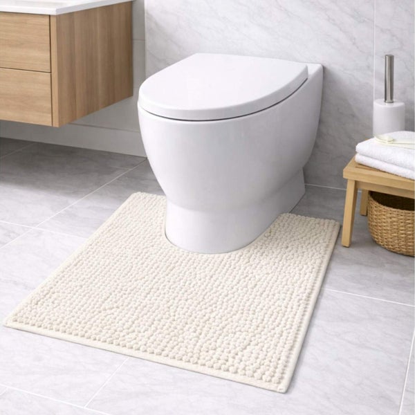 Strukturierte Badematte mit Ausschnitt vor einer Stand-Toilette in einem hellen Badezimmer mit Holzmöbeln und Fliesen in Marmoroptik.
