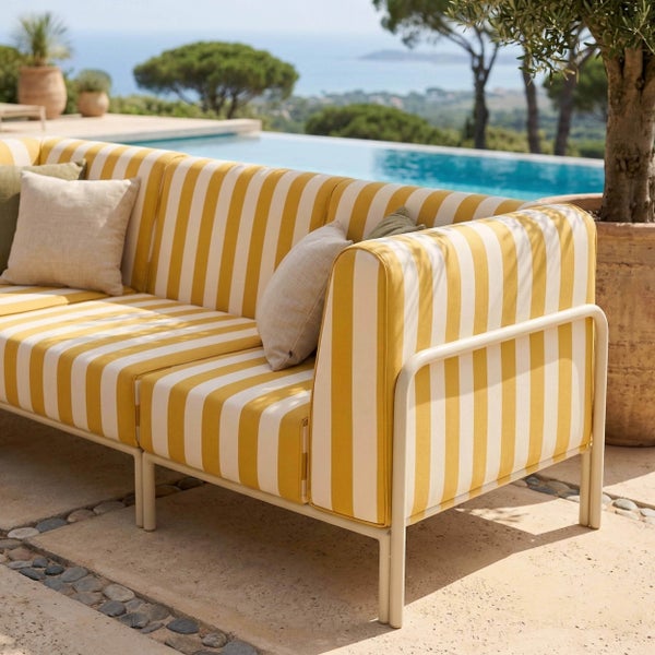 Modernes Loungesofa mit gelb-weiß gestreiften Polstern auf einer hellen Terrasse am Pool mit Meerblick.