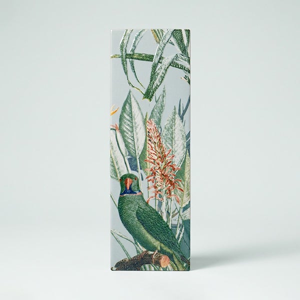Dekorfliese im Format Hochformat mit einem botanischen Dschungelmotiv, das einen Papagei zwischen tropischen Pflanzen und Blüten zeigt.