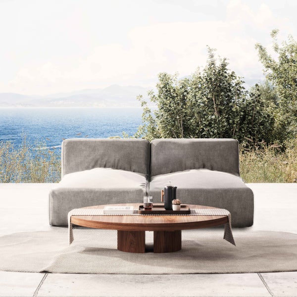 Moderne, helle Terrasse mit einem grauen Loungesofa, einem runden Couchtisch aus Holz auf einem Teppich und weitem Meerblick.