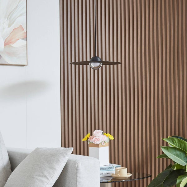 Moderne Pendelleuchte mit flachem Schirm vor einer Wand aus Holzlamellen in einem hellen Wohnzimmer mit Sofa und Dekoration.