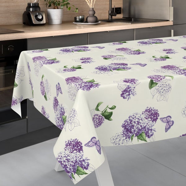 Tischdecke mit Hortensien- und Schmetterlingsmuster auf einem Tisch in einer hellen, modernen Küche mit Holzarbeitsplatte.