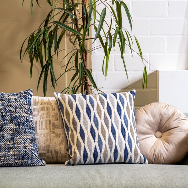 Dekorative Kissen auf einem Sofa mit einer Zimmerpflanze im Hintergrund.