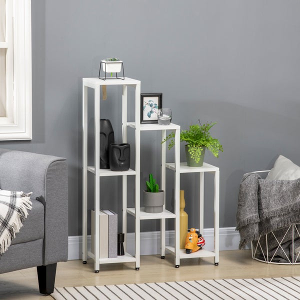 Mehrstufiges weißes Pflanzregal aus Metall in einem Wohnzimmer neben einem grauen Sofa, dekoriert mit Pflanzen, Vasen und Büchern.