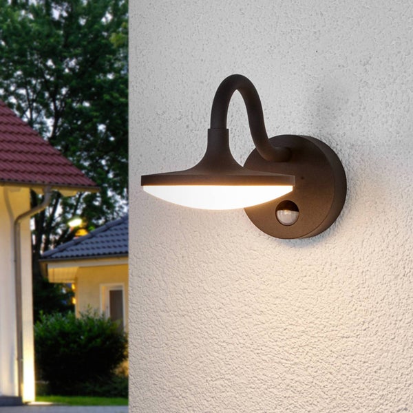 Moderne Außenwandleuchte mit Bewegungsmelder und warmweißem LED-Licht, montiert an einer weißen Hauswand.
