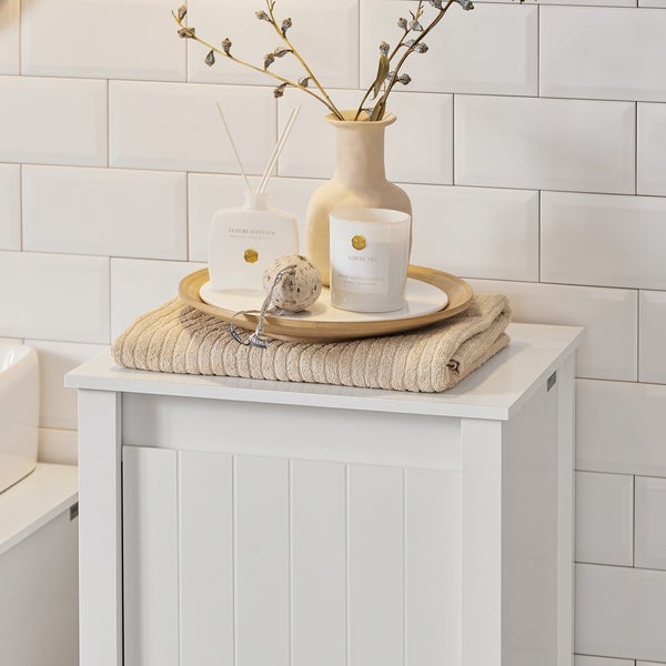 Badezimmer Szene mit weißem Unterschrank, Handtuch, Duftspender, Duftkerze, Vase und Dekoration auf einem Tablett.
