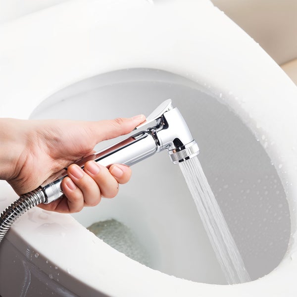 Eine Hand hält eine Bidetdusche über eine Toilettenschüssel, aus der Wasserstrahlen kommen.