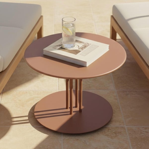Runder terrakottafarbener Metall-Beistelltisch auf einer Terrasse zwischen Loungemöbeln, dekoriert mit einem Buch und einem Glas Wasser.