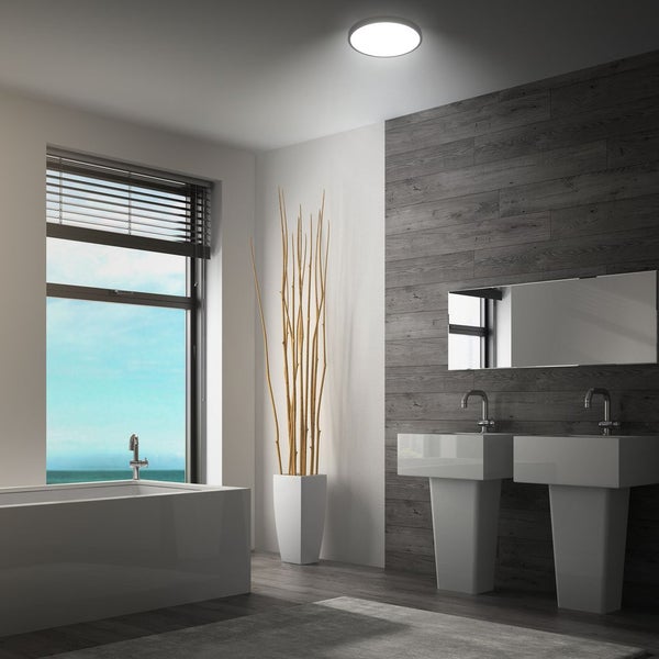 Modernes Badezimmer mit runder Deckenleuchte, zwei Waschbecken, Badewanne und Holzoptik Wandverkleidung bei Tageslicht.