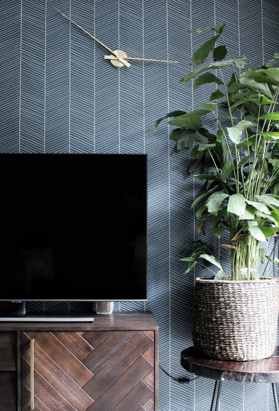 Wohnzimmer mit Fernseher, Kommode, Zimmerpflanze und Wanduhr vor einer Tapete mit Pfeilmuster