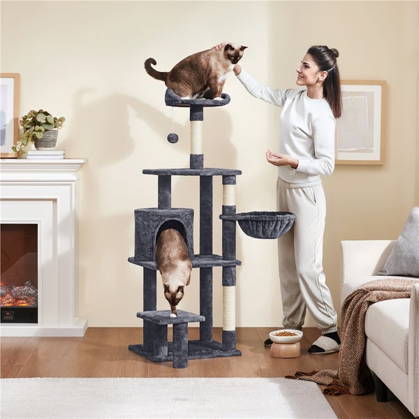 Katzenkratzbaum mit Plattformen, Höhle und Spielzeug in einem Wohnzimmer mit einer Frau, die eine Katze streichelt.