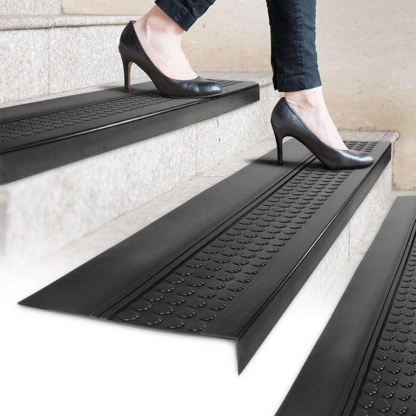 Treppenstufen mit Antirutschprofil und einer Person mit Schuhen mit hohen Absätzen, die die Treppe hinaufgeht.