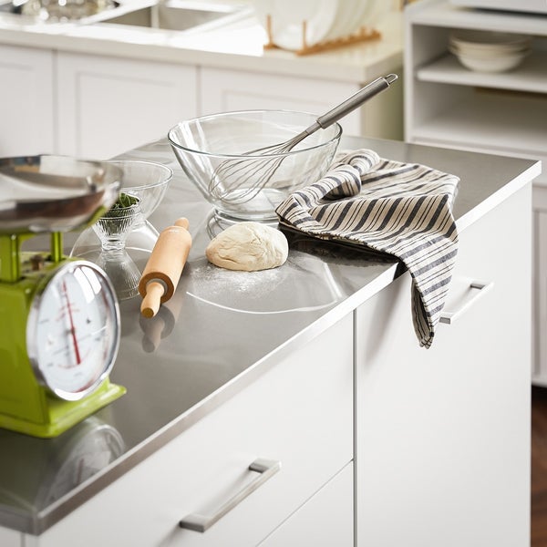 Küchenszene mit Waage, Schüssel, Schneebesen, Teigrolle, Teig und Küchentuch auf einer Arbeitsplatte