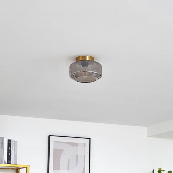 Deckenleuchte mit rauchfarbenem Glasschirm und messingfarbenem Sockel montiert an einer Zimmerdecke.