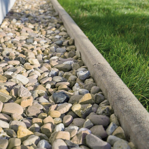 Kiesbett im Garten als Abgrenzung mit einer Steinmauer neben einer Rasenfläche