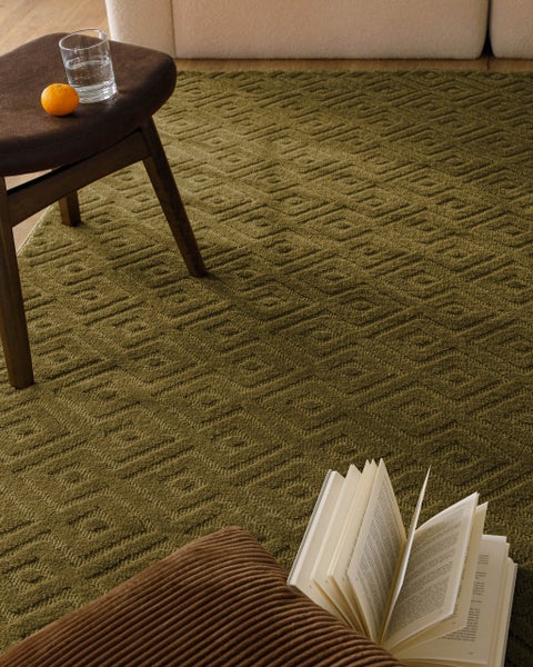 Rechteckiger Teppich mit dezenter Linienstruktur auf Holzboden vor einem Sofa in einem hellen Wohnzimmer.