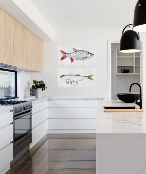 Helle Küche mit Küchenzeile, Kochfeld und Wandbildern mit Fischmotiven.