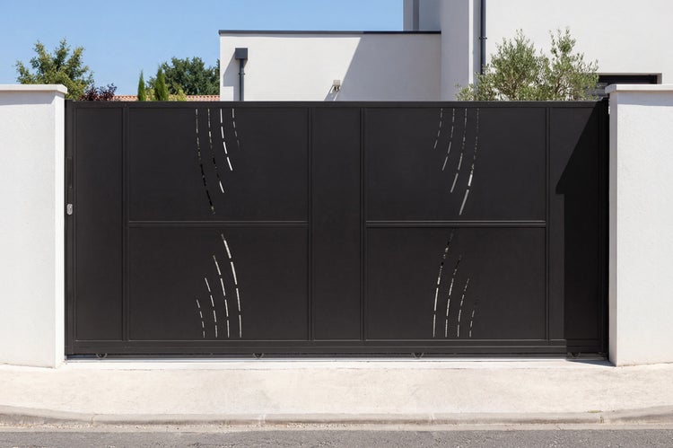 Modernes Schiebetor aus anthrazitfarbenem Aluminium mit dekorativem Muster zwischen weißen Mauern vor einem Wohnhaus.