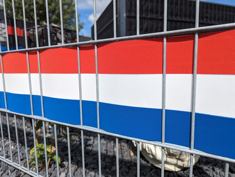 Metallzaun mit rot weiß blau gestreifter Sichtschutzplane