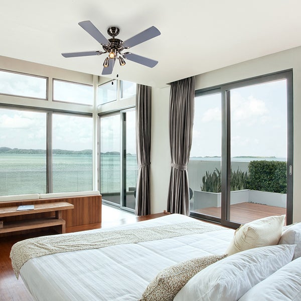 Deckenventilator mit Beleuchtung installiert in einem hellen, modern eingerichteten Schlafzimmer mit großen Fensterfronten und Meerblick.