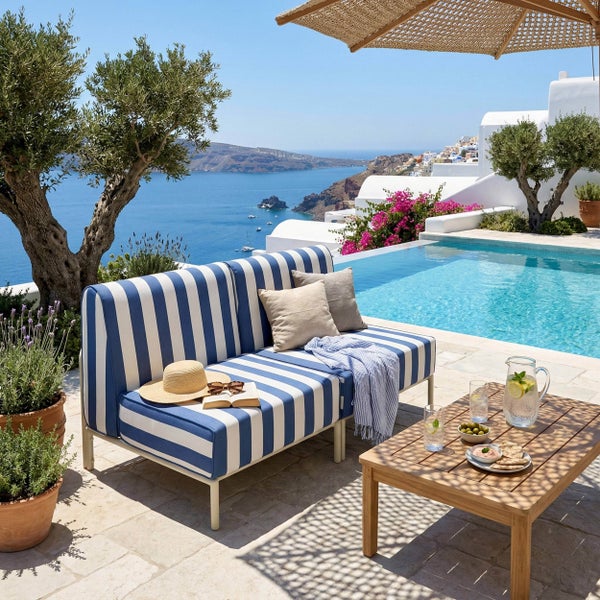 Modernes Gartensofa mit blau-weißen Streifen auf einer hellen Terrasse am Pool mit Meerblick, Holztisch und Olivenbäumen.