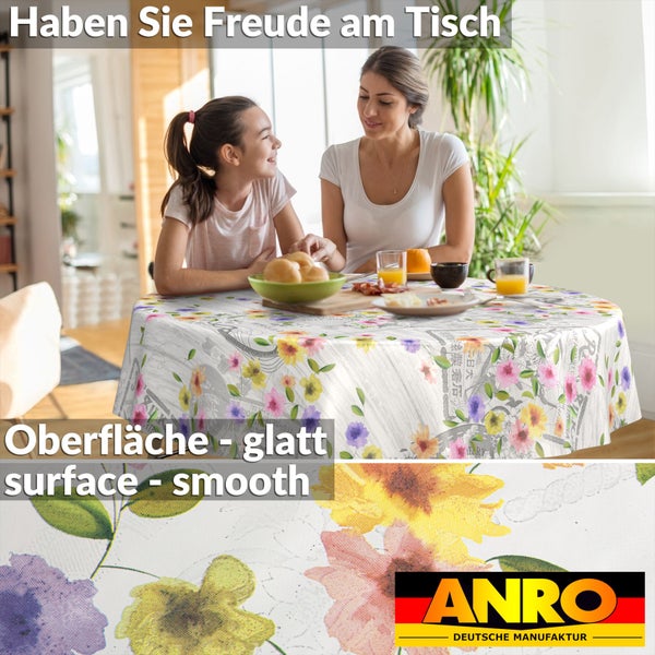 Abwaschbare, runde Tischdecke mit bunten Blumen auf weißem Holzdekor, glatte Oberfläche, in heller Esszimmer-Szene. ANRO Deutsche Manufaktur Logo.
