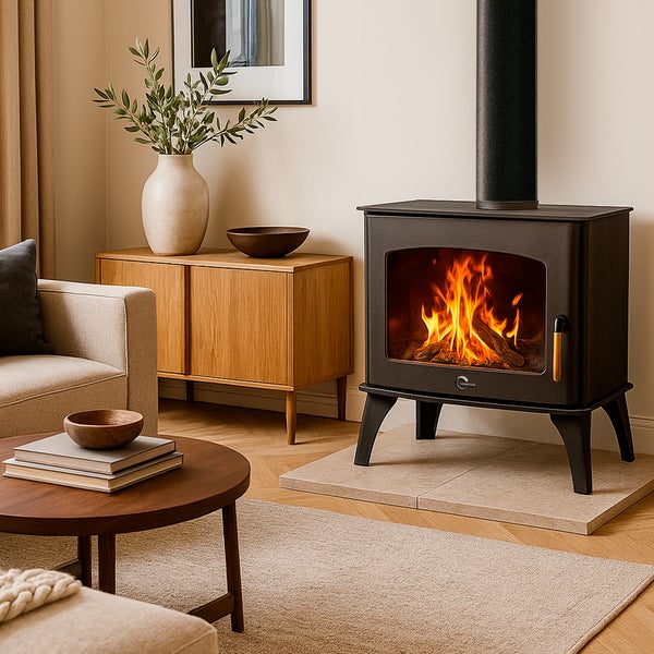 Schwarzer Kaminofen mit brennendem Feuer im hellen Wohnzimmer auf einer Steinplatte neben einem Sideboard aus Holz.