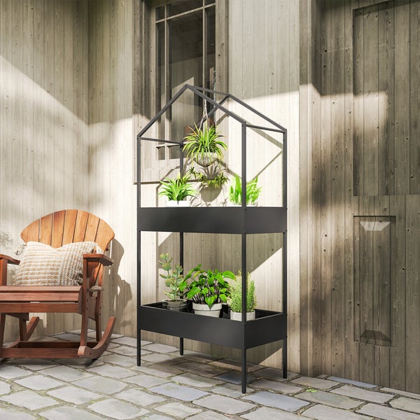 Pflanzenregal aus Metall in Hausform mit zwei Ebenen auf einer hellen Terrasse neben einem Holzschaukelstuhl vor einer Holzwand.