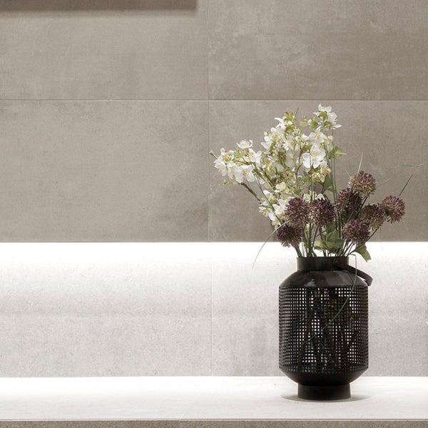 Wandfliesen im modernen Stil vor einer indirekt beleuchteten Wand mit einer dekorativen Blumenvase aus Metallgitter.