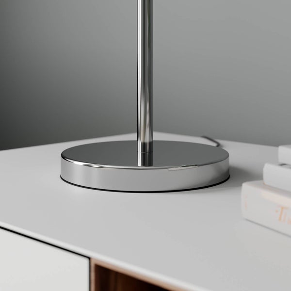 Detailaufnahme einer Tischleuchte mit verchromtem Fuß auf einem weißen Nachttisch