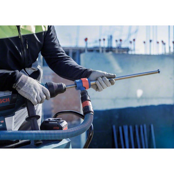 Ein Mann bedient einen Bohrhammer mit Absaugvorrichtung auf einer Baustelle.