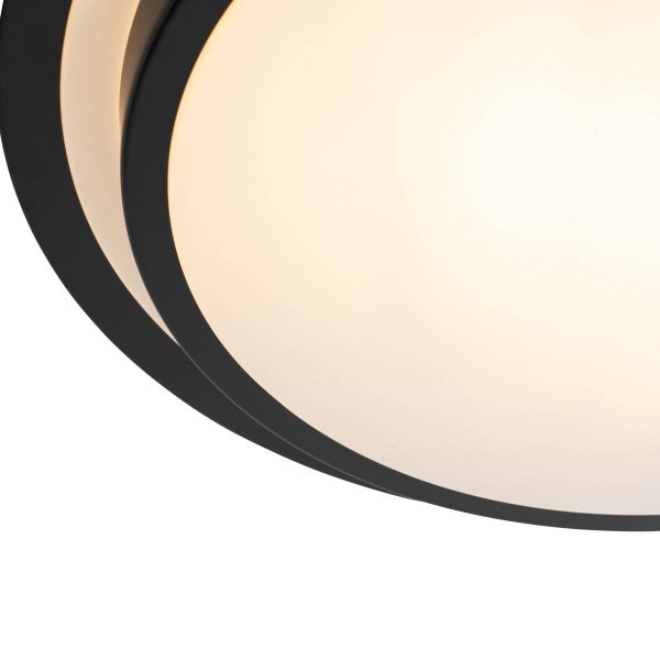 Runde Deckenleuchte mit schwarzem Rahmen und weißem Diffusor, Detailansicht im eingeschalteten Zustand.