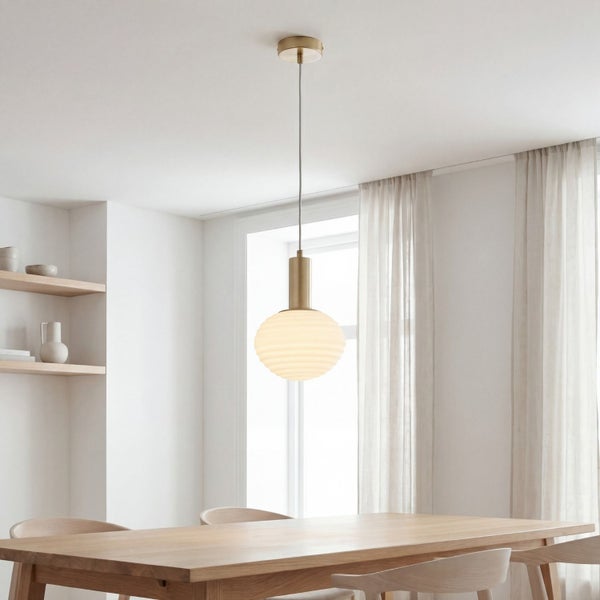 Moderne Pendelleuchte mit geriffeltem Glas und Messingfassung in hellem, minimalistischem Esszimmer mit Holztisch und Vorhängen.