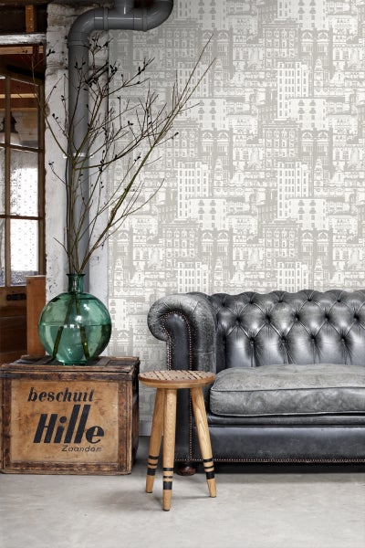 Wohnzimmer mit grauer Ledercouch, Holzhocker und bedruckter Tapete