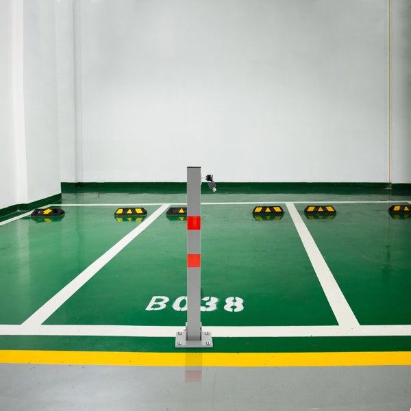 Quadratischer Parkpfosten aus Metall mit roten Reflexstreifen und Schloss in einer Tiefgarage auf grünem Boden montiert.