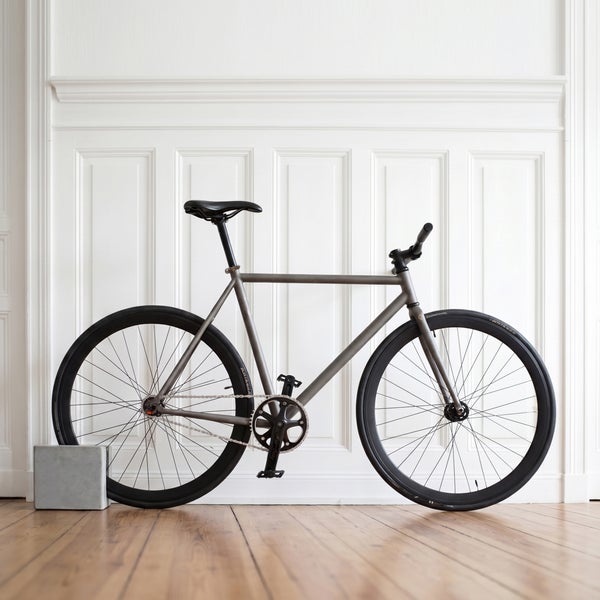 Graues Fahrrad vor einer Wand mit Kassettenverkleidung auf einem hellen Holzboden.