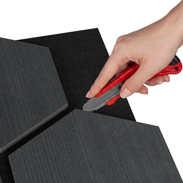 Eine Hand schneidet mit einem Cuttermesser ein dunkles, sechseckiges Akustikpaneel zu.