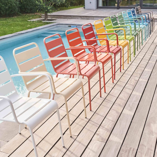 Mehrere farbenfrohe Garten-Stapelsessel aus Metall mit Armlehnen auf einer Holzterrasse an einem Pool.