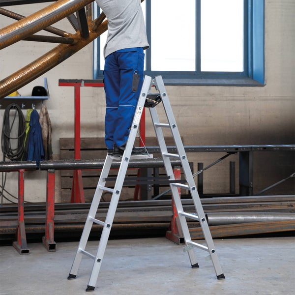 Eine Person steht auf einer Aluminium-Doppelleiter in einer Werkstatt.