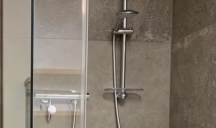 Moderne Duscharmatur mit Brausestange und Ablage in einer gefliesten Dusche mit Glaswand.