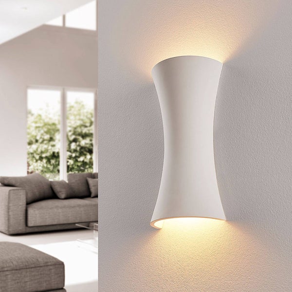 Moderne weiße Wandleuchte in Sanduhrform mit Lichtaustritt nach oben und unten an einer Wand in einem hellen, modern eingerichteten Wohnzimmer.
